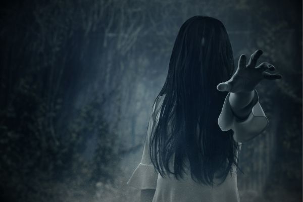 Scary women with long black hair covering her face in a dark wooded area.